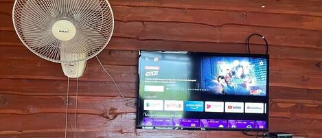Un televisor montado en una pared de madera con un ventilador a su lado.