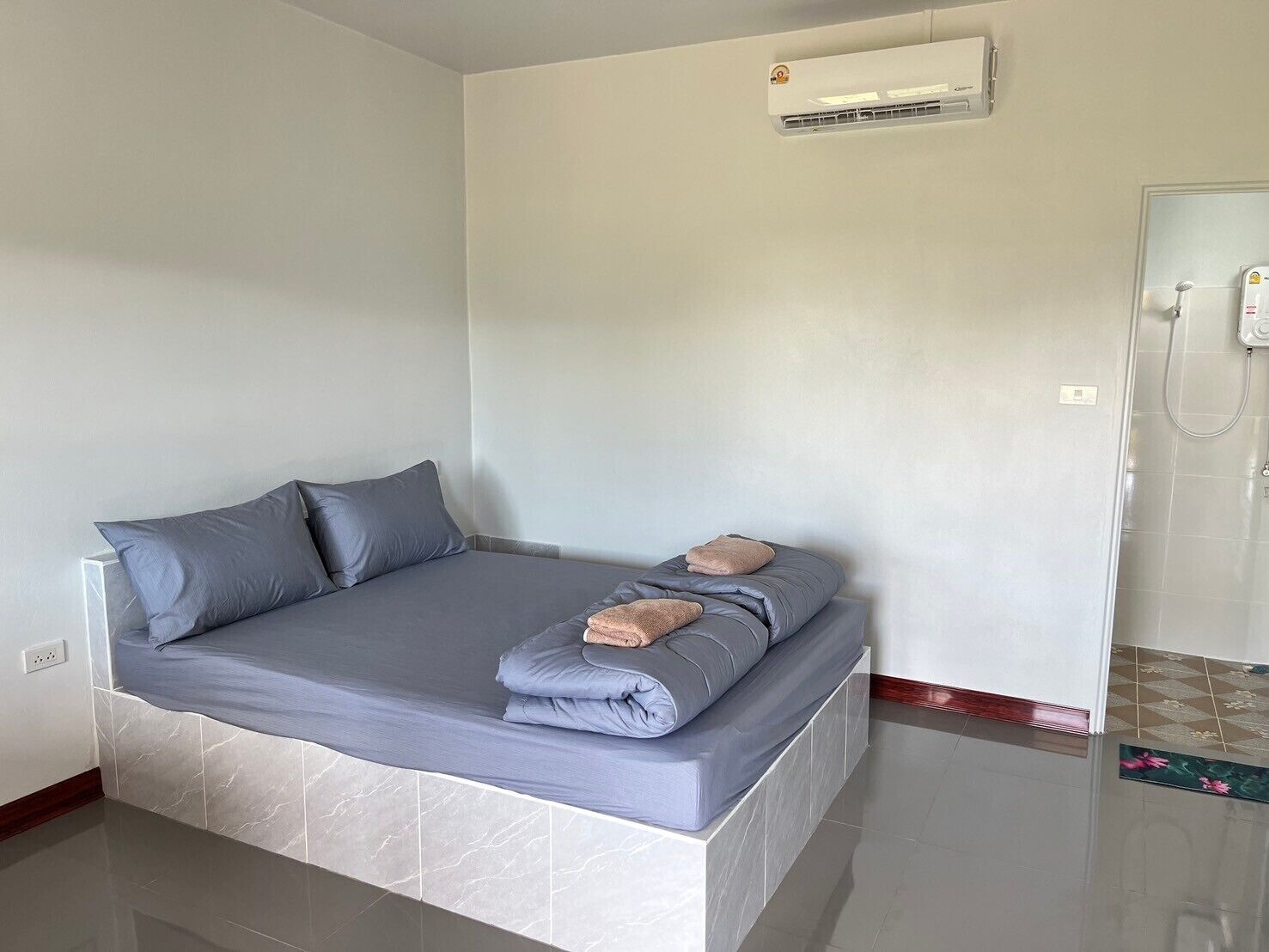 A small, modern room with a bed, a shower, and an air conditioning unit on the wall.