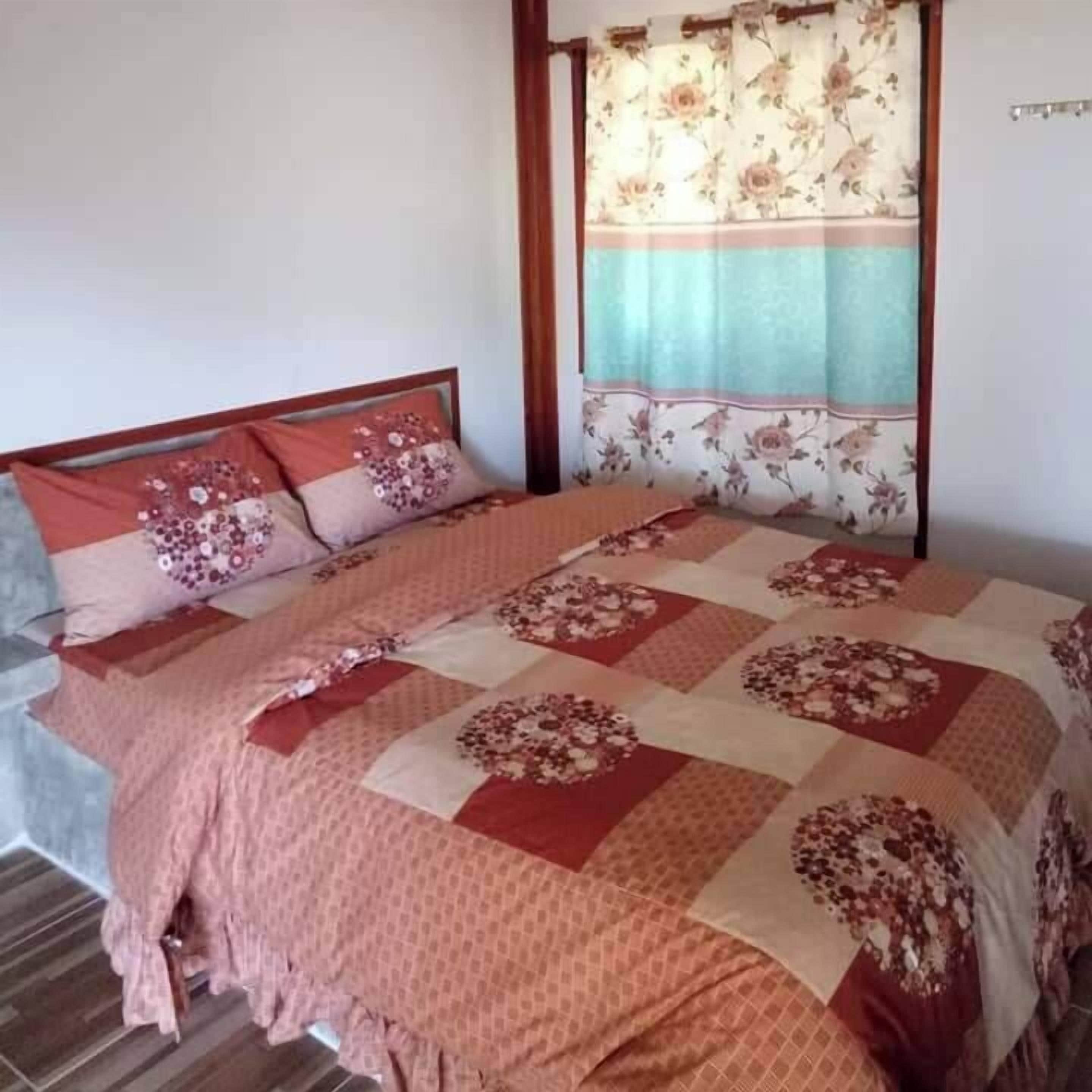 Quarto com cama, cortinas florais e colcha estampada.