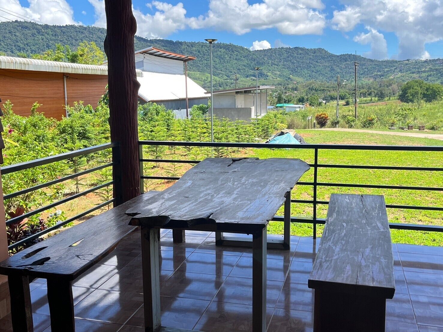 A terrace with a wooden table and benches, overlooking a green landscape and hills.