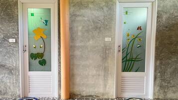 Dos puertas con paneles de vidrio esmerilado que presentan diseños florales, una pared con textura y un suelo de baldosas con dos felpudos.