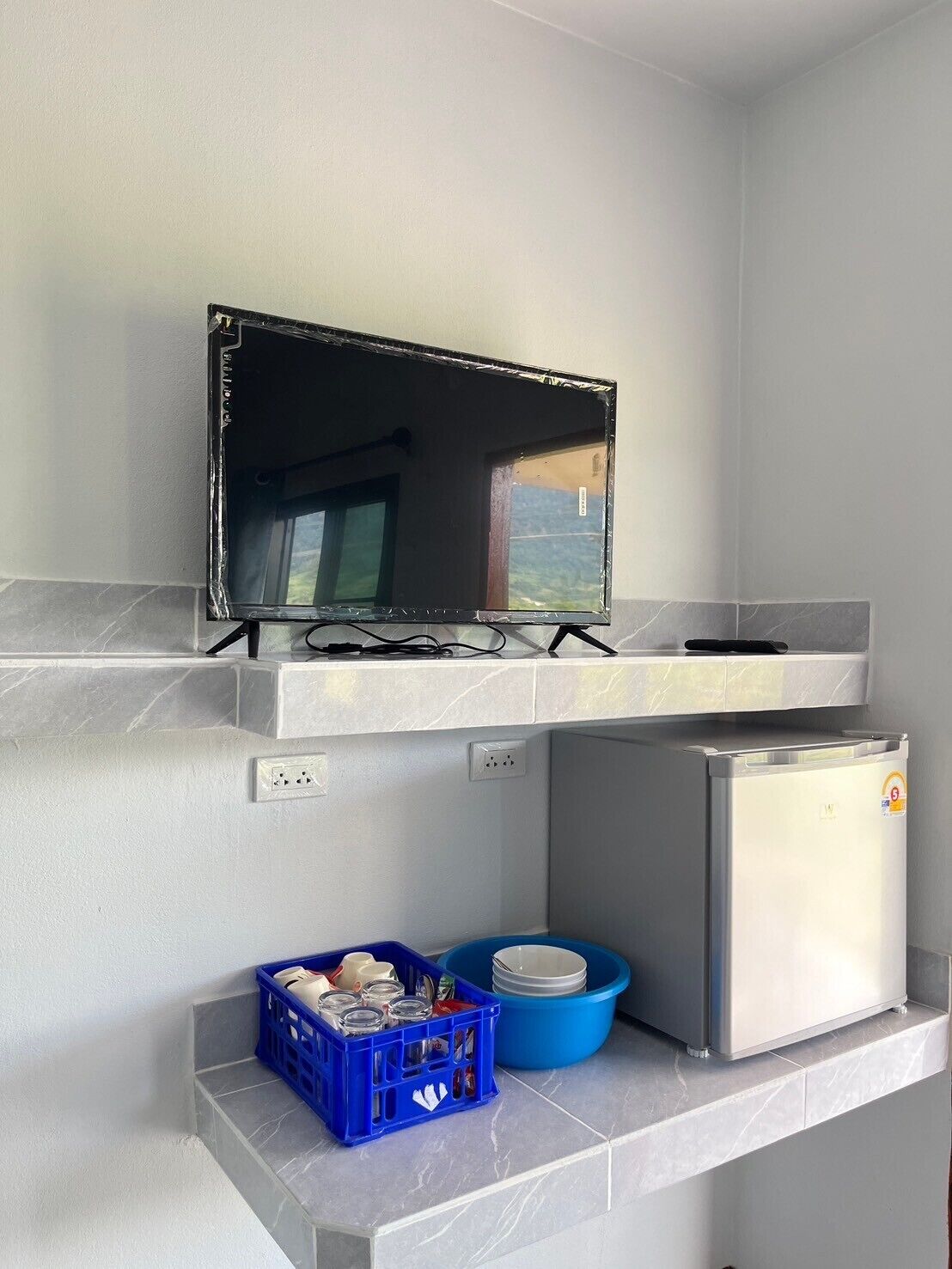 A kitchen with a TV mounted on a shelf, a refrigerator, and a blue storage bin with dishes.