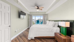 Een slaapkamer met een bed, een plafondventilator, een televisie, een nachtkastje en uitzicht op de omgeving.