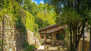 Eine rustikale Holzhütte mit Steinwand, Holzterrasse und Essbereich mit Gartenmöbeln.