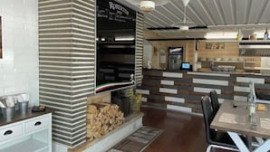 Un interior de restaurante moderno con una chimenea central, suelo de madera y una barra con un tablero de menú.
