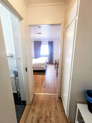 A narrow hallway leading to a bedroom with a bed, a window with curtains, and a small table. - Lamar hotel (Angelholm)
