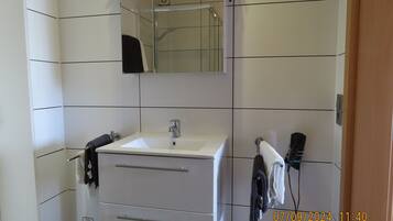 A bathroom with white tiled walls, a white sink with a mirror above it, and a towel rack with towels.