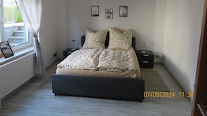 Een slaapkamer met een bed, twee nachtkastjes, een raam met gordijnen, en drie ingelijste foto's aan de muur.