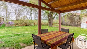 A covered outdoor seating area with a table and chairs, surrounded by a wooden fence and trees. - Comfortable 2-bedroom cottage with garden, pets allowed, Wifi, parking (Montilliers)