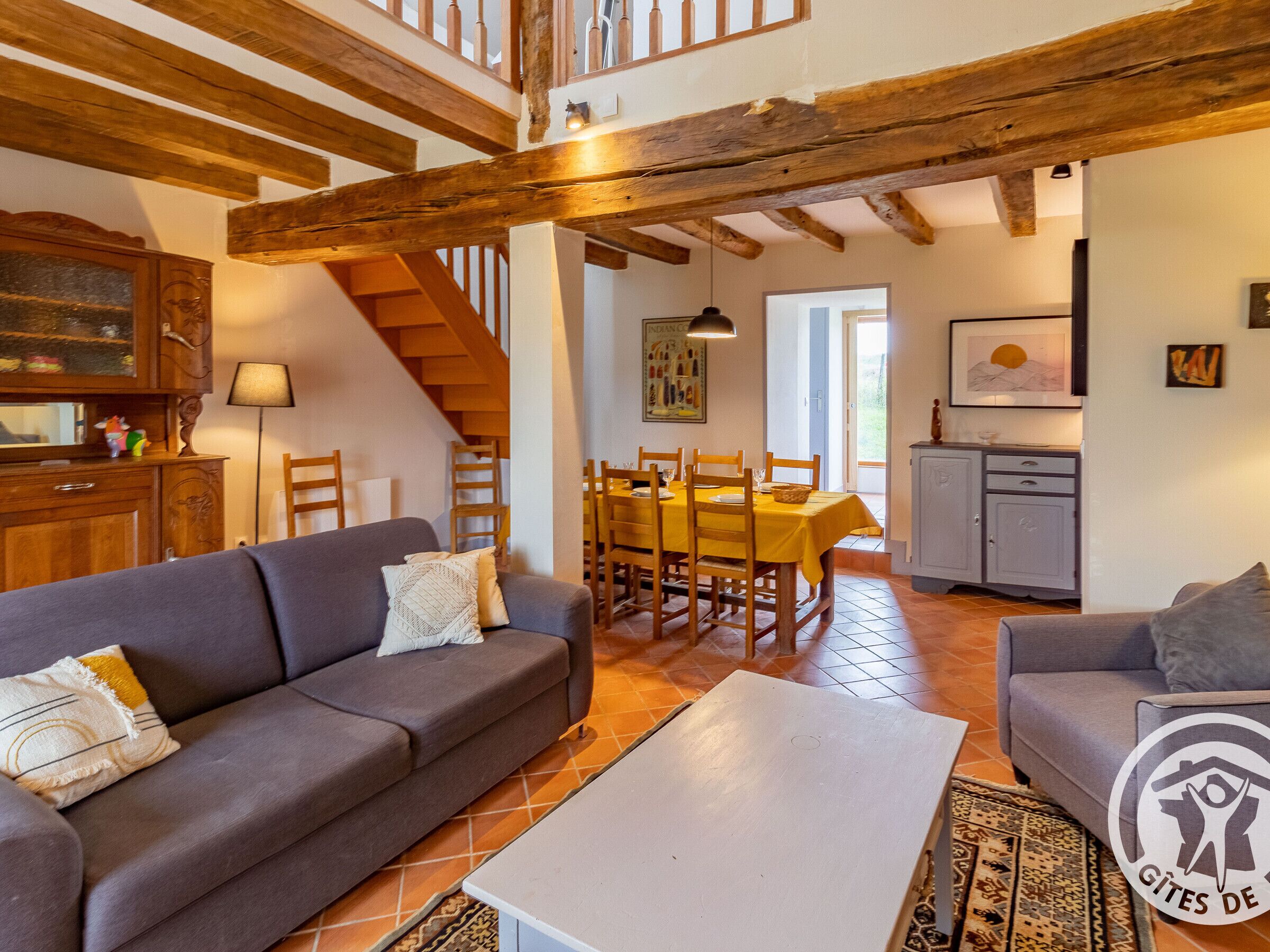 Una sala de estar acogedora con un sofá, una mesa de centro y un comedor con sillas y una mesa. Una escalera conduce a un nivel superior.
