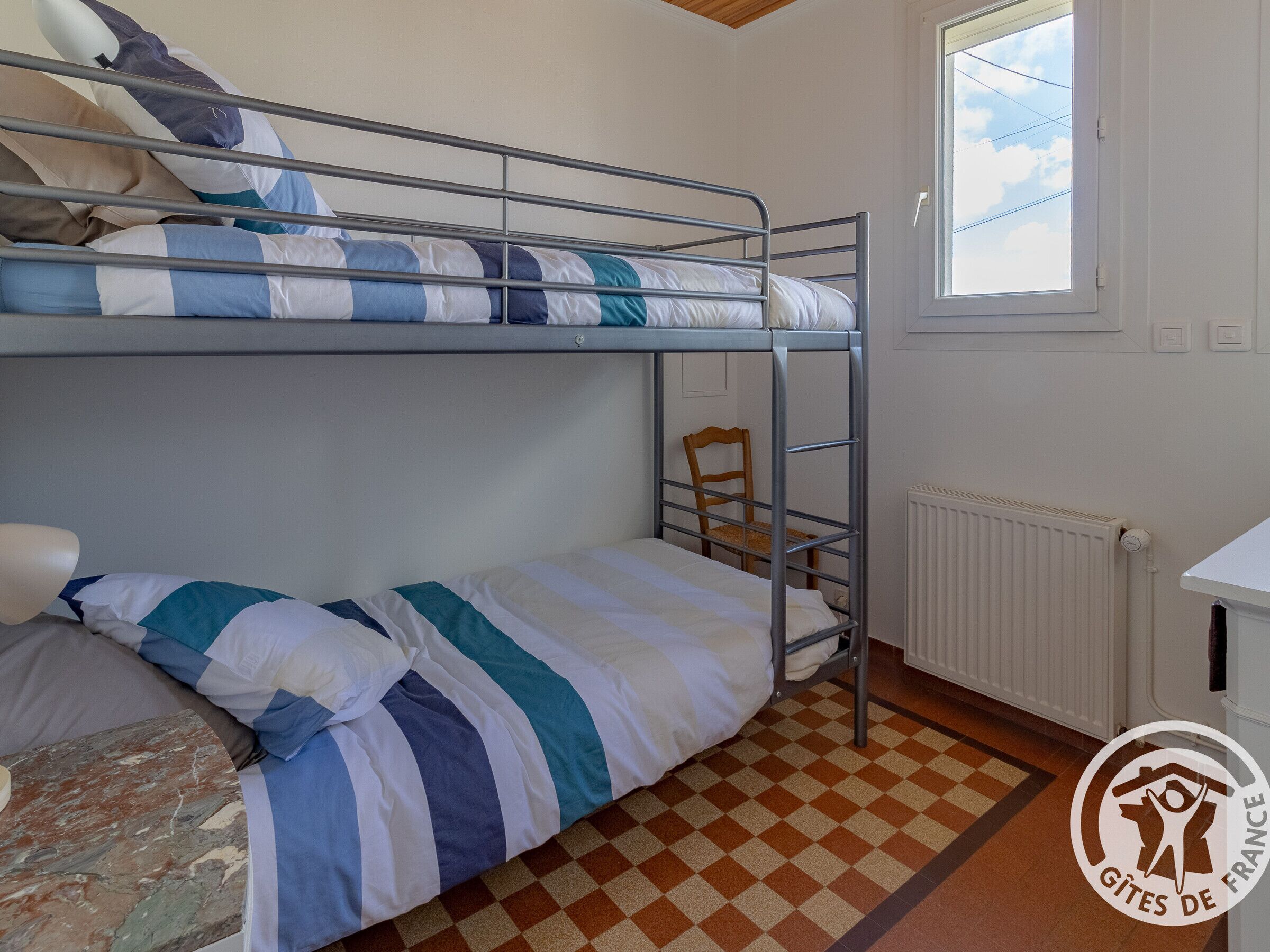 Un dormitorio con literas, una silla, un radiador y una ventana que da al cielo.