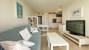 Una sala de estar moderna con sofá, mesa de centro, televisor y una cocina al fondo.