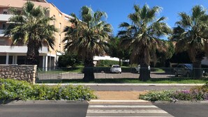 Un estacionamiento con palmeras y un edificio al fondo.