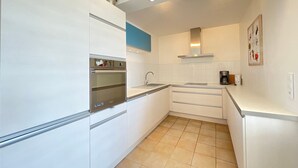 Una cocina moderna con armarios blancos, horno empotrado, pileta y cafetera.