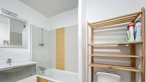 Un baño con ducha, inodoro y un estante con artículos de aseo.