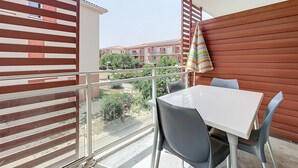 Un balcón con mesa y sillas, una toalla a rayas y vistas a edificios y zonas verdes.