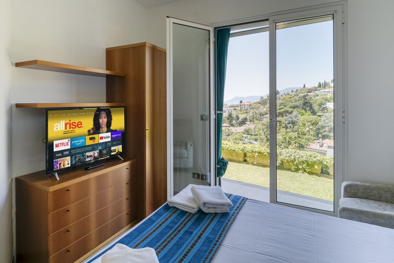 Une chambre avec un lit, un téléviseur posé sur une commode en bois, un balcon avec vue et une porte-fenêtre coulissante.
