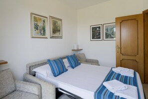 A bedroom with a bed, two pillows, a bedside table, a chair, and a door.