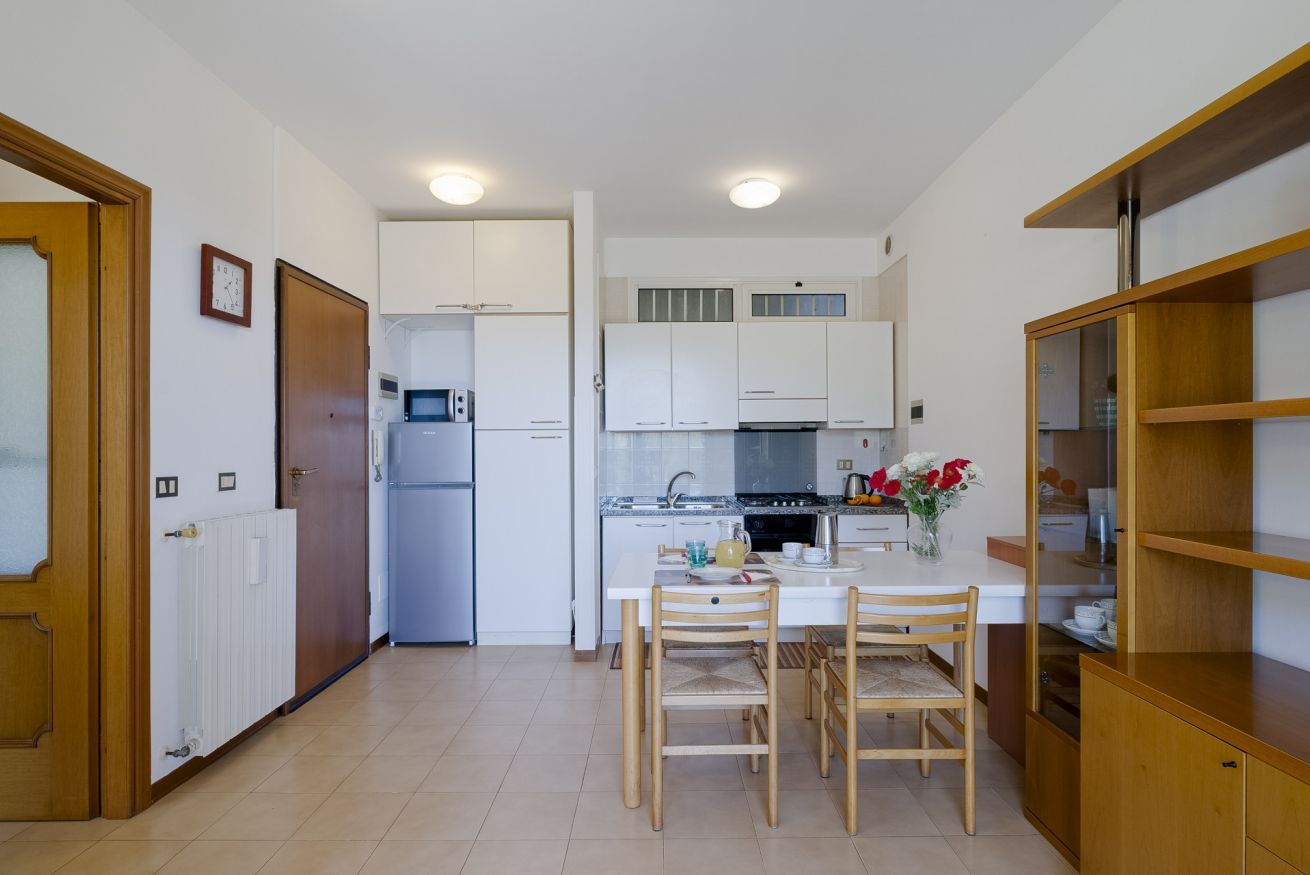 Una cucina compatta con mobili bianchi, un frigorifero, un piano cottura e un'area pranzo con tavolo e sedie.