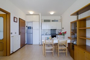 Cocina compacta con armarios blancos, un refrigerador, estufa y comedor con mesa y sillas.