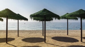 A beach with three thatched umbrellas and a clear view of the sea.