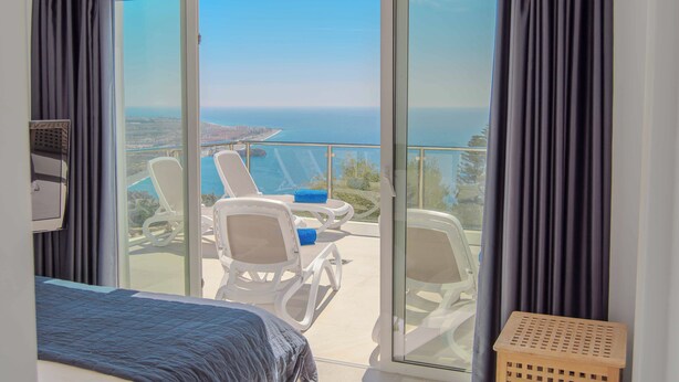 A balcony with a bed, two white chairs, and a view of the sea.