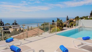 A poolside area with lounge chairs and a glass balustrade overlooking the sea.