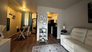 En moderne stue med en beige sofa, et spiseområde med bord og stole, og et køkken i baggrunden.
