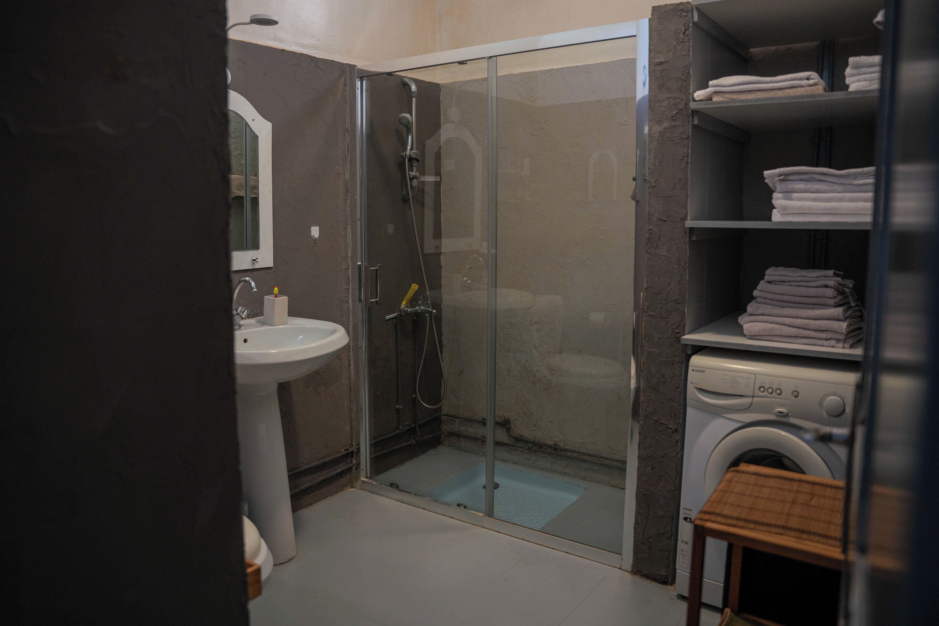A bathroom with a glass-enclosed shower, a sink, and a stacked laundry area.