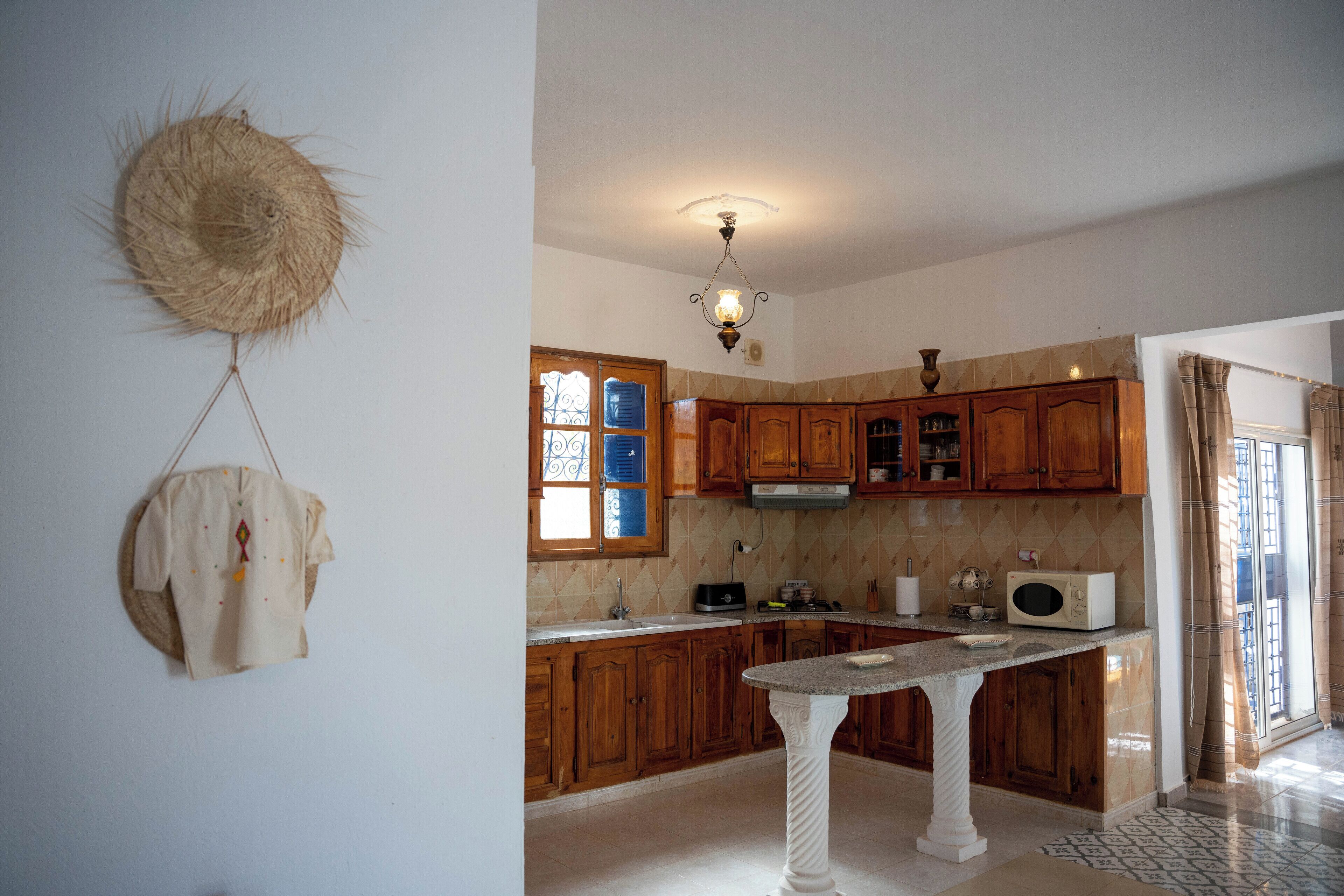 Una cocina con armarios de madera, una encimera blanca, un adorno colgante y una lámpara en el techo.