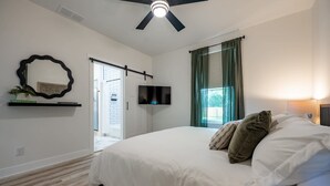 Ein Schlafzimmer mit einem Bett, einem an der Wand montierten Fernseher, einem Deckenventilator und einem Fenster mit Vorhängen.