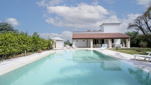 A swimming pool with lounge chairs, a covered area, and a building with a tiled roof. - GuestHost - Magnificent villa with pool, bright and with large outdoor spaces, located in a quiet residential area between Torre a Mare and Noicattaro. Iit comfortably accommodates up to 8 people and is furnished with refined taste. Perfect for those loo (Parco Scizzo-Parchitello)