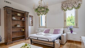 A bedroom with a bed, a sofa, a wooden cabinet, a chandelier, and a window with curtains. - GuestHost - Magnificent villa with pool, bright and with large outdoor spaces, located in a quiet residential area between Torre a Mare and Noicattaro. Iit comfortably accommodates up to 8 people and is furnished with refined taste. Perfect for those loo (Parco Scizzo-Parchitello)
