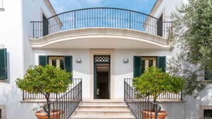 A two-story building with a curved balcony, a central entrance with a door, and two potted trees on either side of the entrance. - GuestHost - Magnificent villa with pool, bright and with large outdoor spaces, located in a quiet residential area between Torre a Mare and Noicattaro. Iit comfortably accommodates up to 8 people and is furnished with refined taste. Perfect for those loo (Parco Scizzo-Parchitello)
