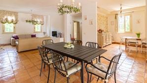 A dining area with a table and chairs, a sofa, and a TV in a room with tiled flooring and a chandelier. - GuestHost - Magnificent villa with pool, bright and with large outdoor spaces, located in a quiet residential area between Torre a Mare and Noicattaro. Iit comfortably accommodates up to 8 people and is furnished with refined taste. Perfect for those loo (Parco Scizzo-Parchitello)