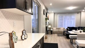 Eine moderne Küche mit Einbauofen, ein Essbereich mit Tisch und Stühlen sowie ein Wohnzimmer mit Sofa und Couchtisch.