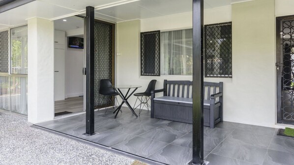 A modern outdoor seating area with a sofa and chairs, a small table, and a TV screen mounted on the wall.