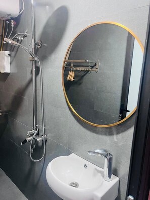 Bathroom features a pedestal sink, round mirror, and shower area with handheld showerhead.