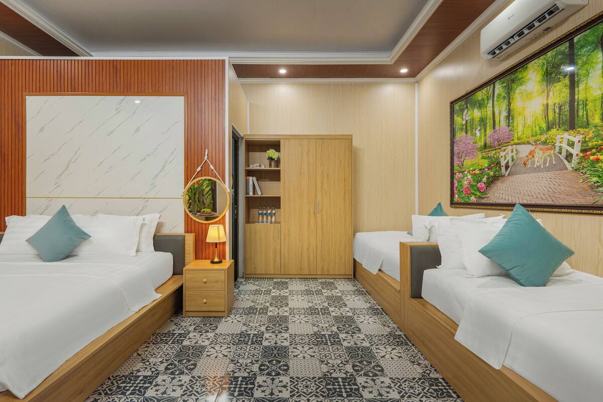 A hotel room with two beds, a wardrobe, a small table with a lamp, and a large painting on the wall.