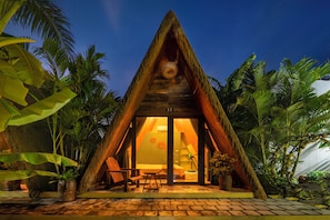 A triangular-shaped building with a thatched roof, surrounded by tropical plants.