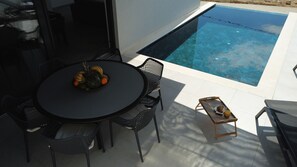 A poolside area with a round table, chairs, and a fruit bowl.