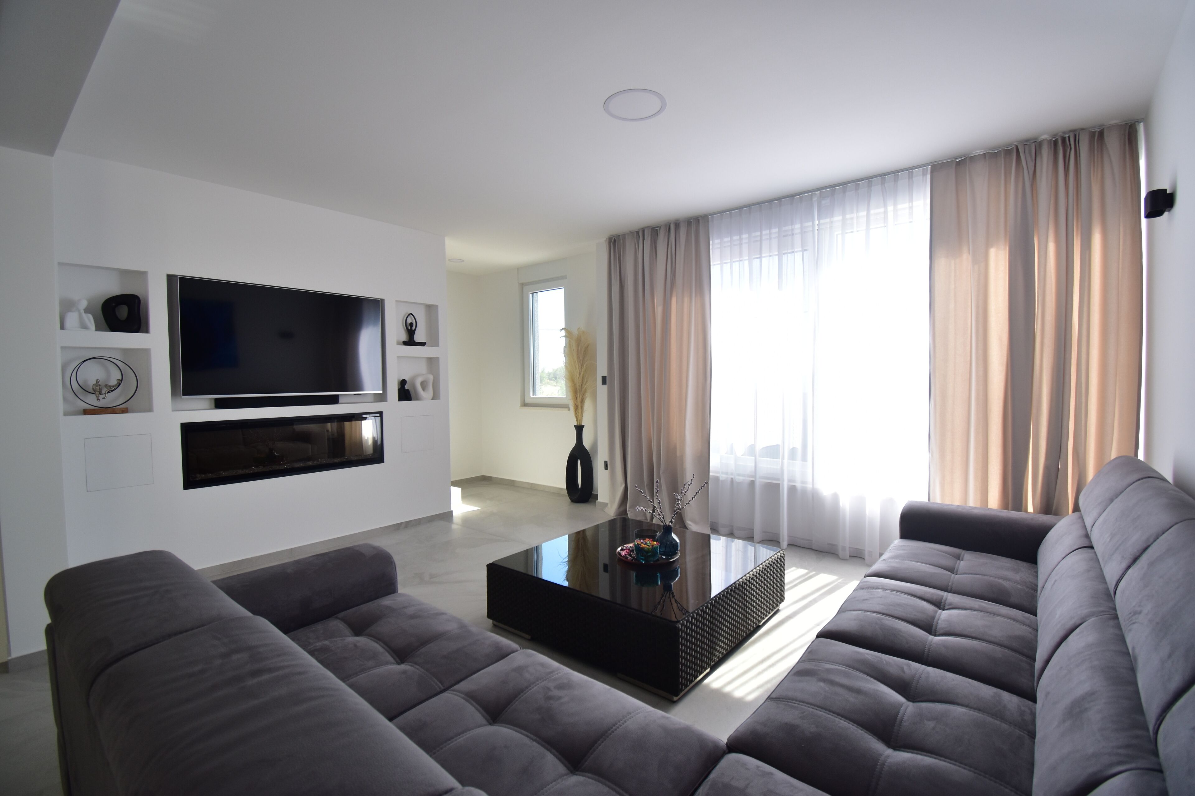 A modern living room with a flat-screen TV, a black coffee table, and two grey sofas.