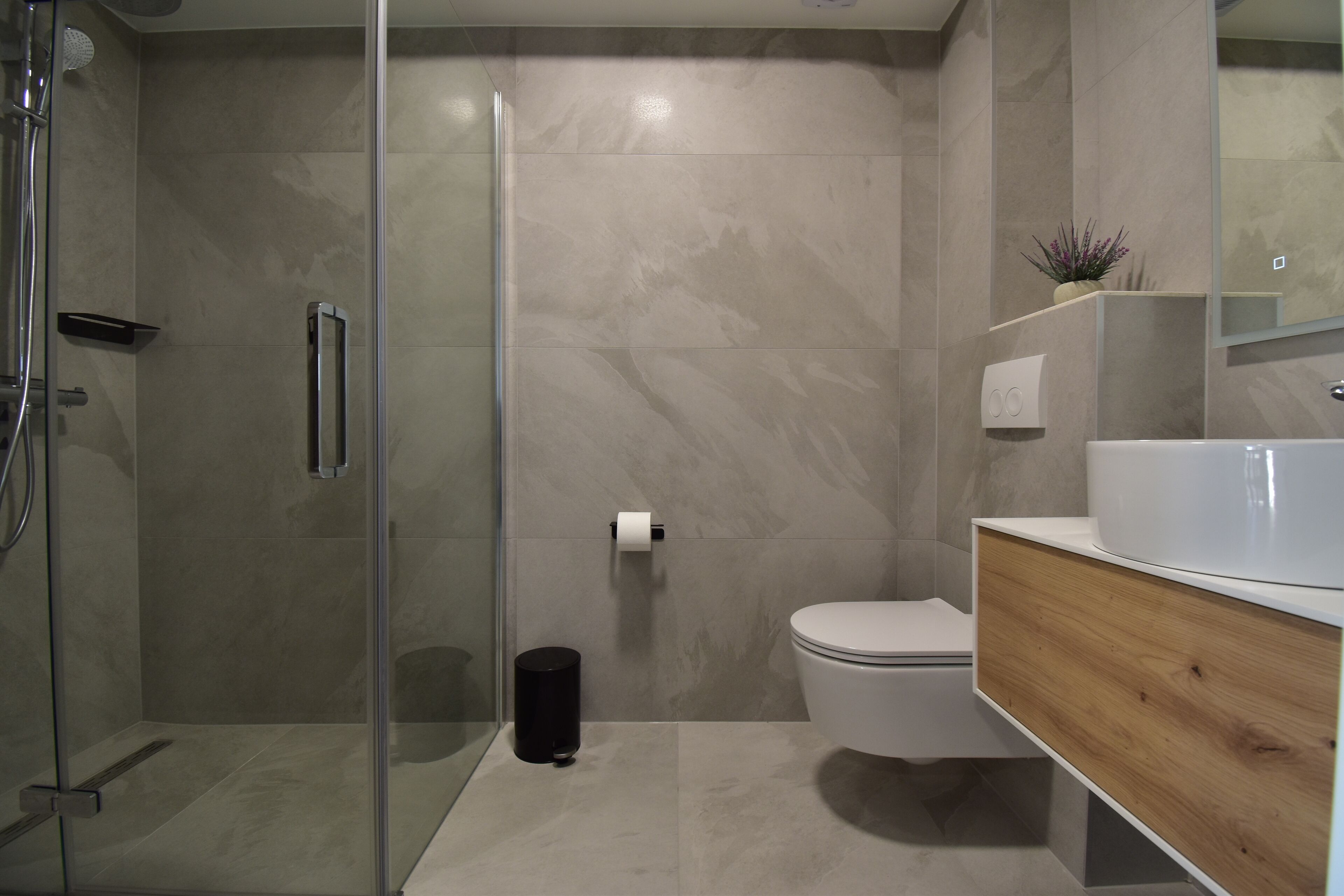 Une salle de bain moderne dotée d’une douche à parois de verre, de toilettes et d’un meuble-lavabo avec un miroir.