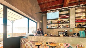 A bar area with a menu board, shelves of bottles, stools, and a counter. - Ostello Bello Palermo  (Palermo)