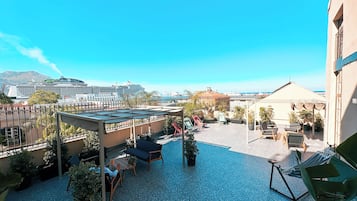 A rooftop patio with outdoor seating, potted plants, and a view of the sea and cruise ships.