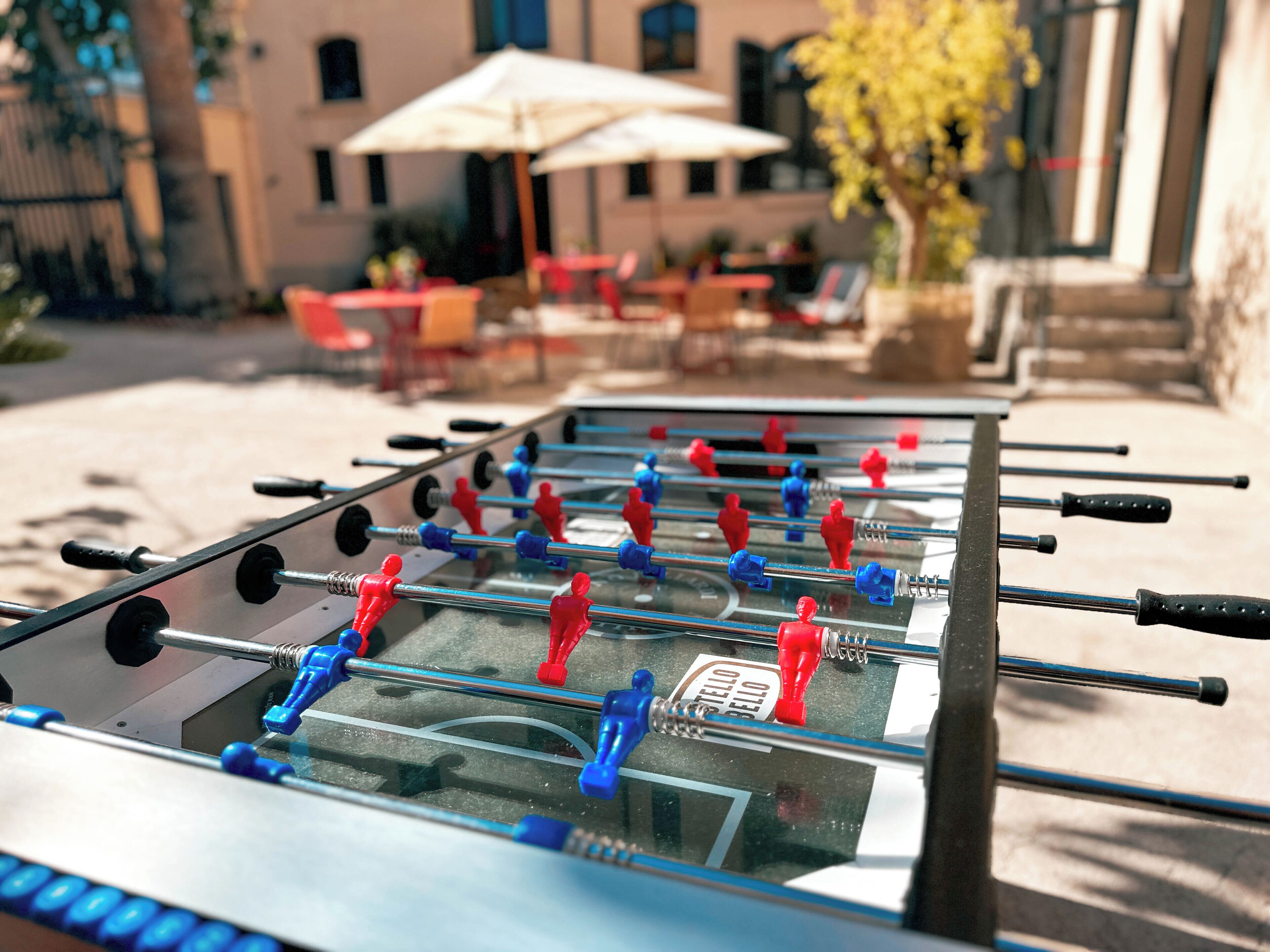 Una mesa de fútbol de mesa en un entorno al aire libre, con mesas y sillas al fondo.