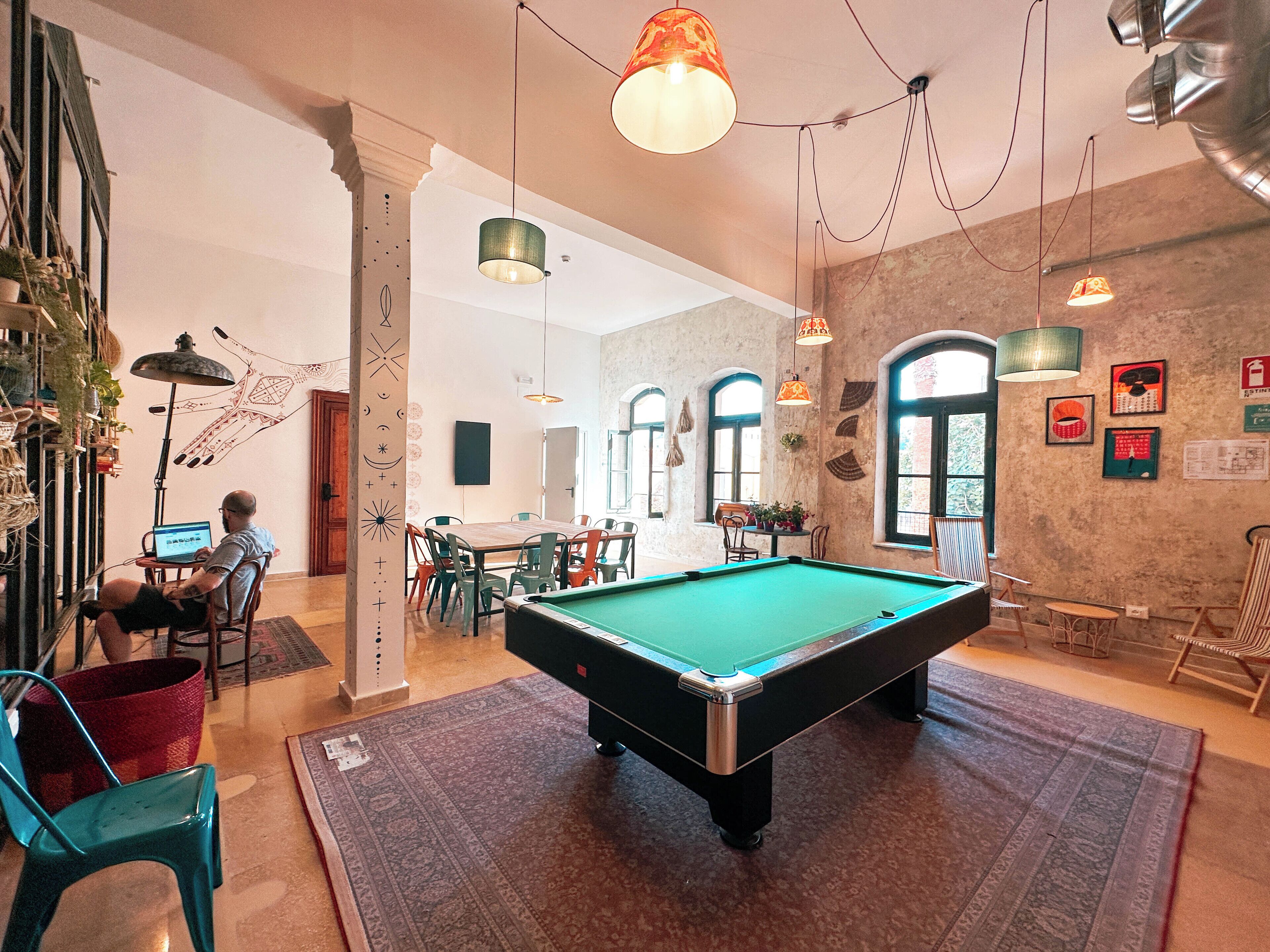 A pool table in a room with a rustic brick wall, a wooden dining table, and hanging pendant lights.