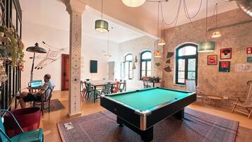 A pool table in a room with a rustic brick wall, a wooden dining table, and hanging pendant lights.