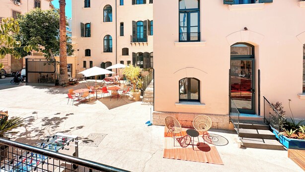 A courtyard with outdoor seating, a foosball table, and a palm tree. - Ostello Bello Palermo  (Palermo)