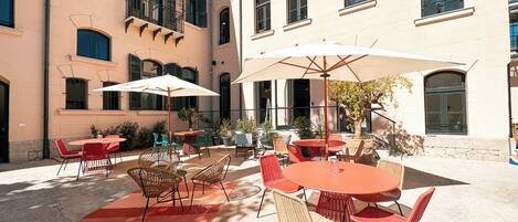 An outdoor patio area with round tables and chairs, umbrellas, and potted plants.